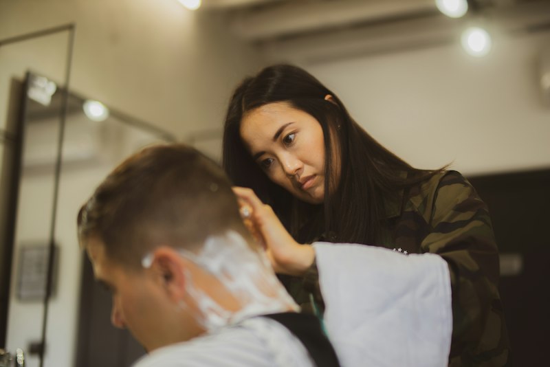 A female barber concentrating as she finishes a client's neckline with a straight razor