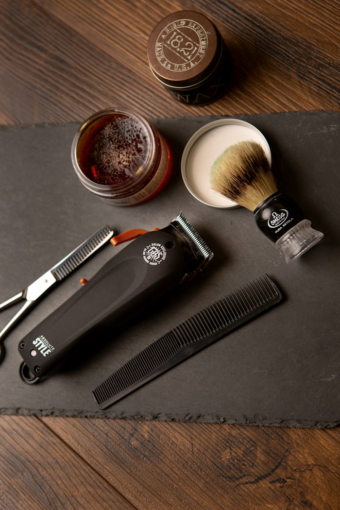 A shaving brush, clipper, comb and pomade laid out on slate over walnut boards